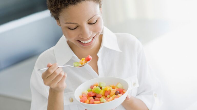 A woman smiles down at a bowl full of colorful fruit. Image demonstrates foods that boost your metabolism.