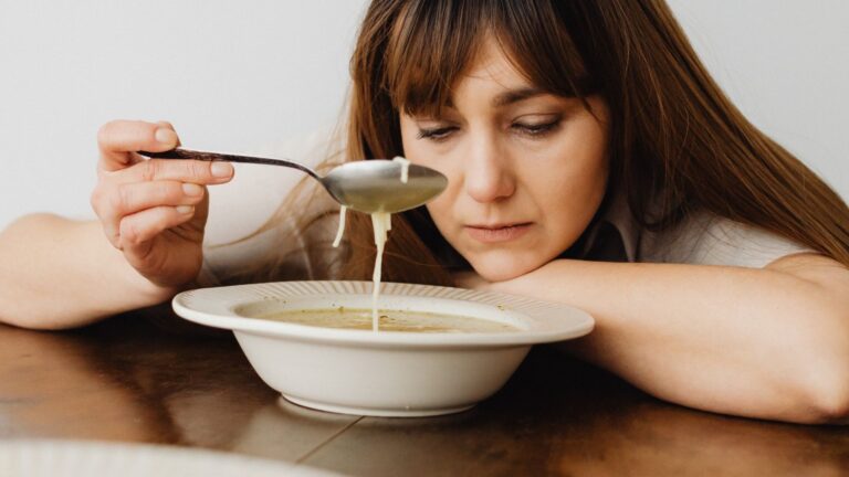 A woman frowns down at her bowl of soup, dissatisfied with it. Image demonstrates how a calorie deficit diet is not satisfying.