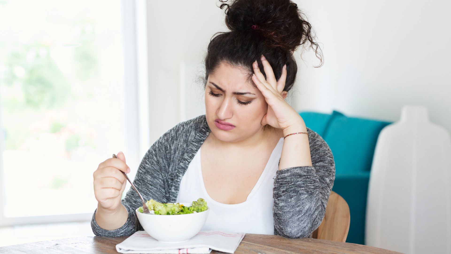 A woman frowns down at her salad, dissatisfied. Picture illustrates how a calorie deficit diet might be harmful.
