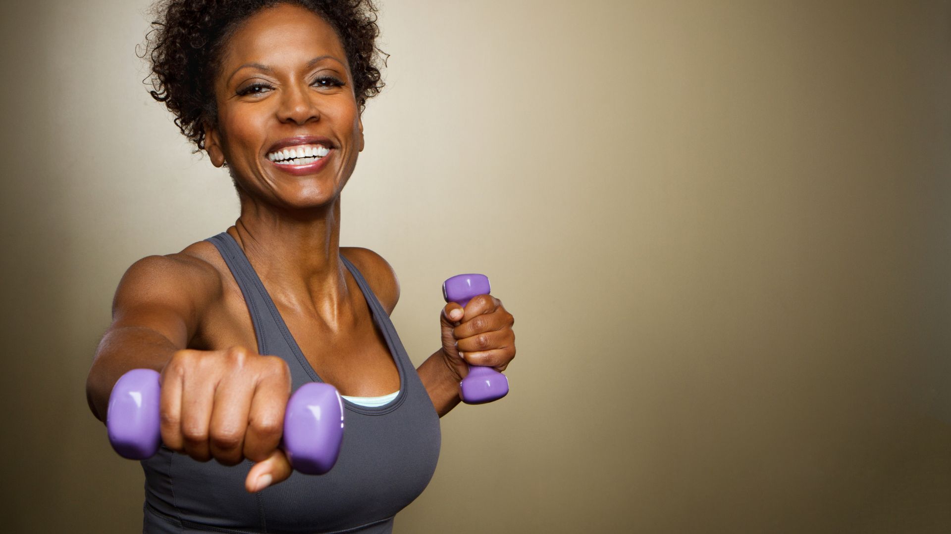 A woman holding weights smiles as she exercises. Image demonstrates examples of diet and exercise.