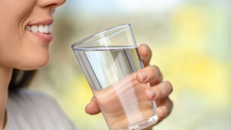 A woman smiles as she's drinking water.