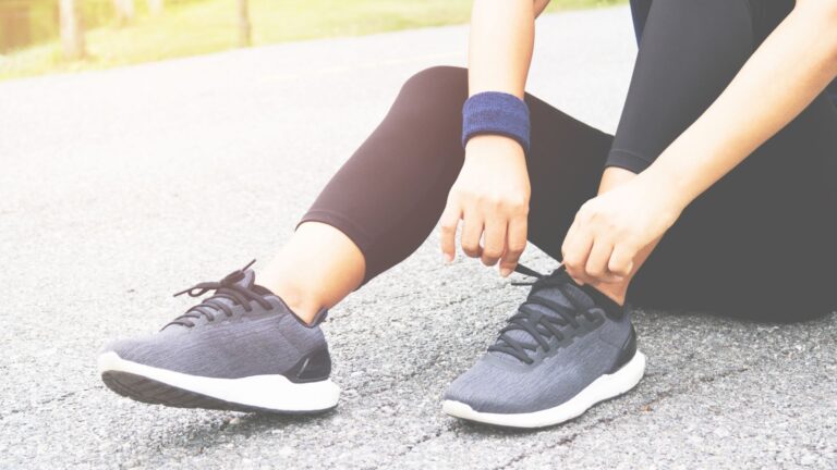 A woman sits on the pavement and laces up her sneakers. Image demonstrates how many of us are exercising for weight loss.