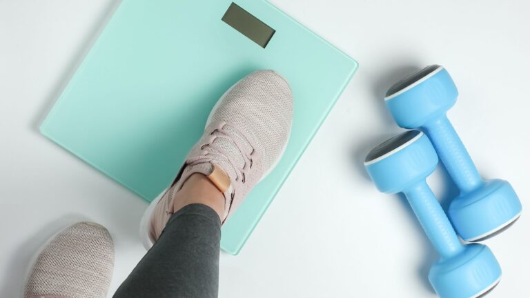 A woman is seen stepping onto a scale with her sneaker, and there are blue weights next to her. Image demonstrates how weight loss is impeded by hormonal imbalances.