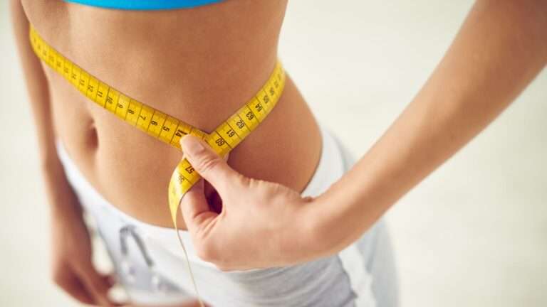 A woman stands with a measuring tape around her waist. Image demonstrates the results of losing weight permanently.