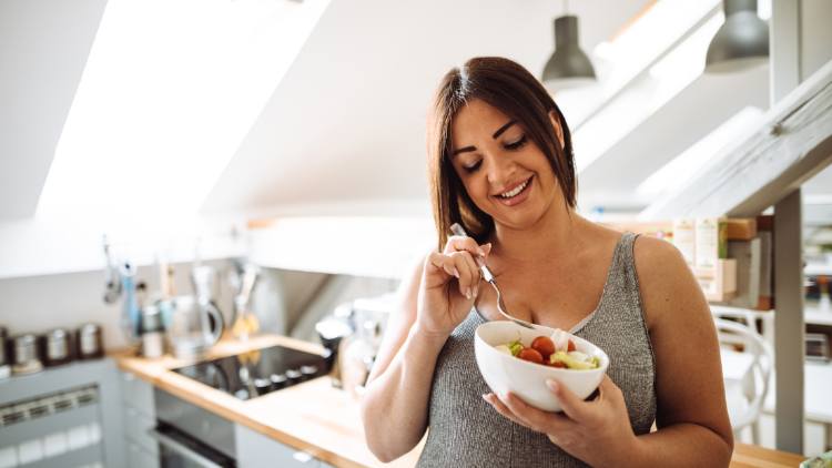 A woman eating healthy food in the kitchen in an effort to lose weight fast.