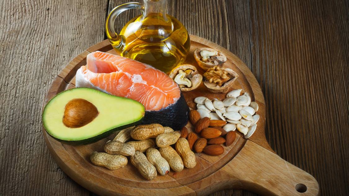 A plate of food on a wooden board that show examples of healthy fats.