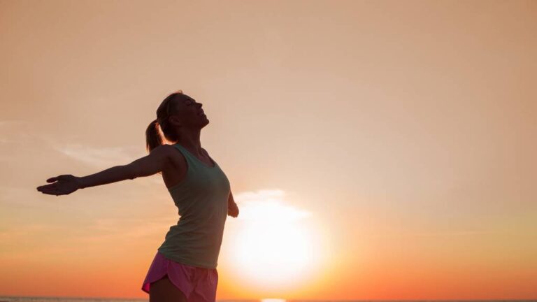 A woman in a sunset silhoutte celebrating the loss of 100 lbs by following The Metabolism Reboot plan.