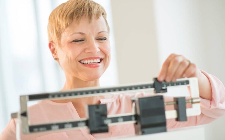 An older woman measuring herself on the scale to see if her intermittent fasting is working for weight loss.