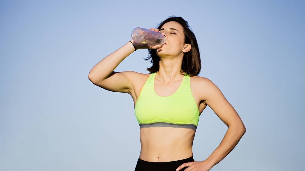 A female, standing outside with workout clothes on, drinking water to show its importance in weight loss.