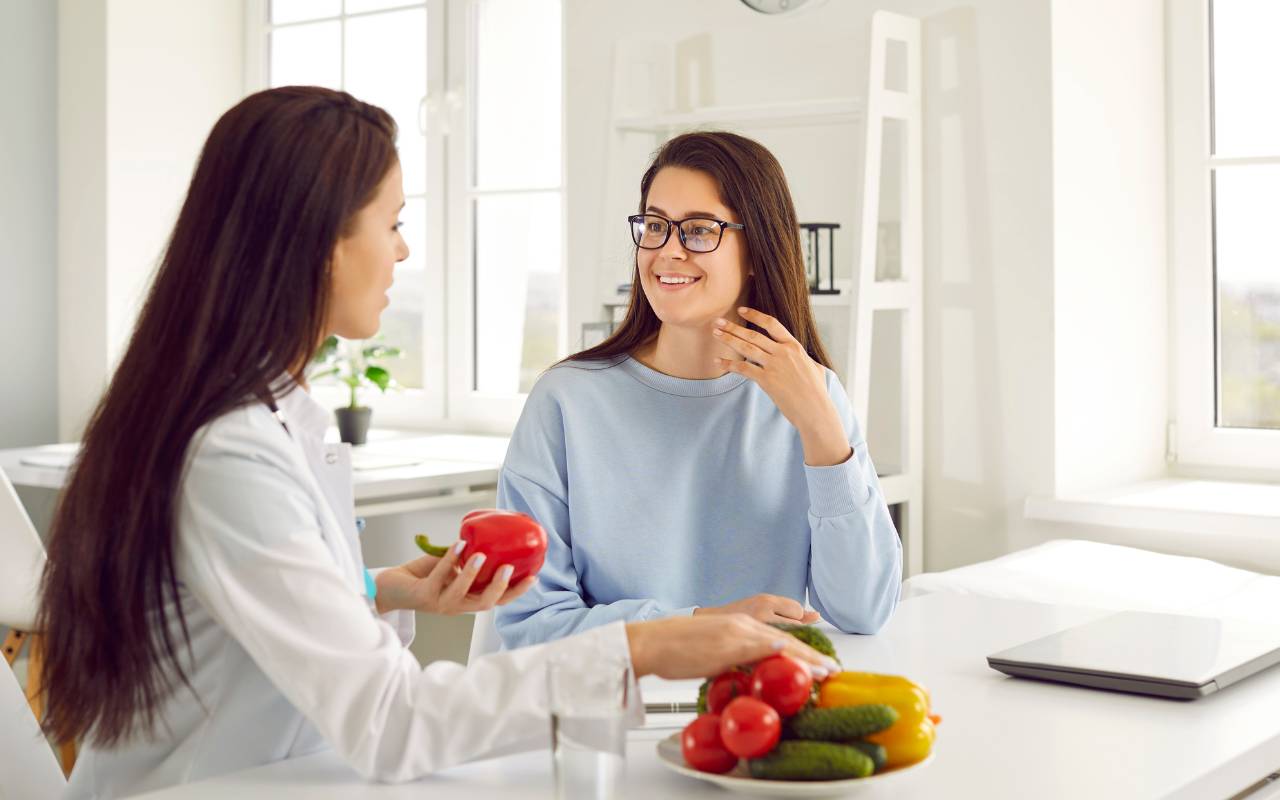 Two women discussing how to control your appetite by using healthy food on a table as the example.