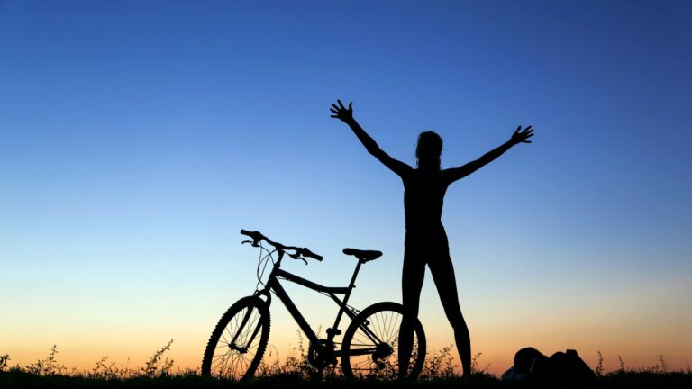 person standing next to bike in sunset with arms raised