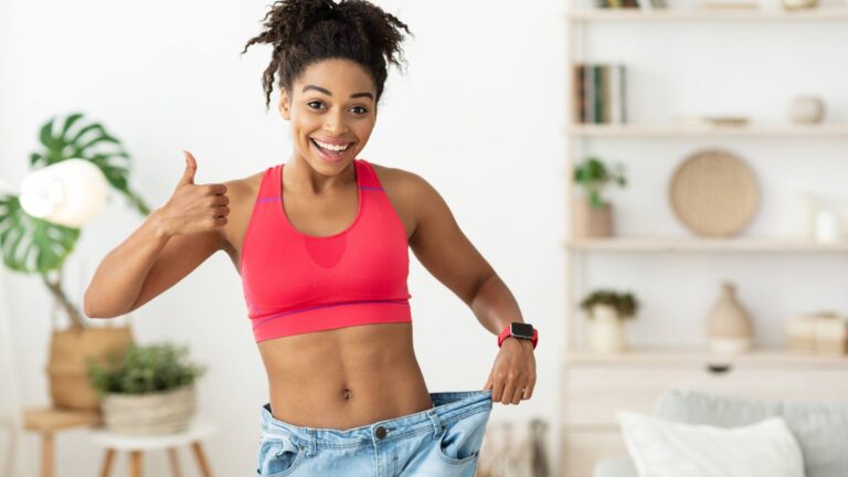An image of a woman holding her baggy pants out and posing a thumbs up. She is demonstrating that losing weight is possible.