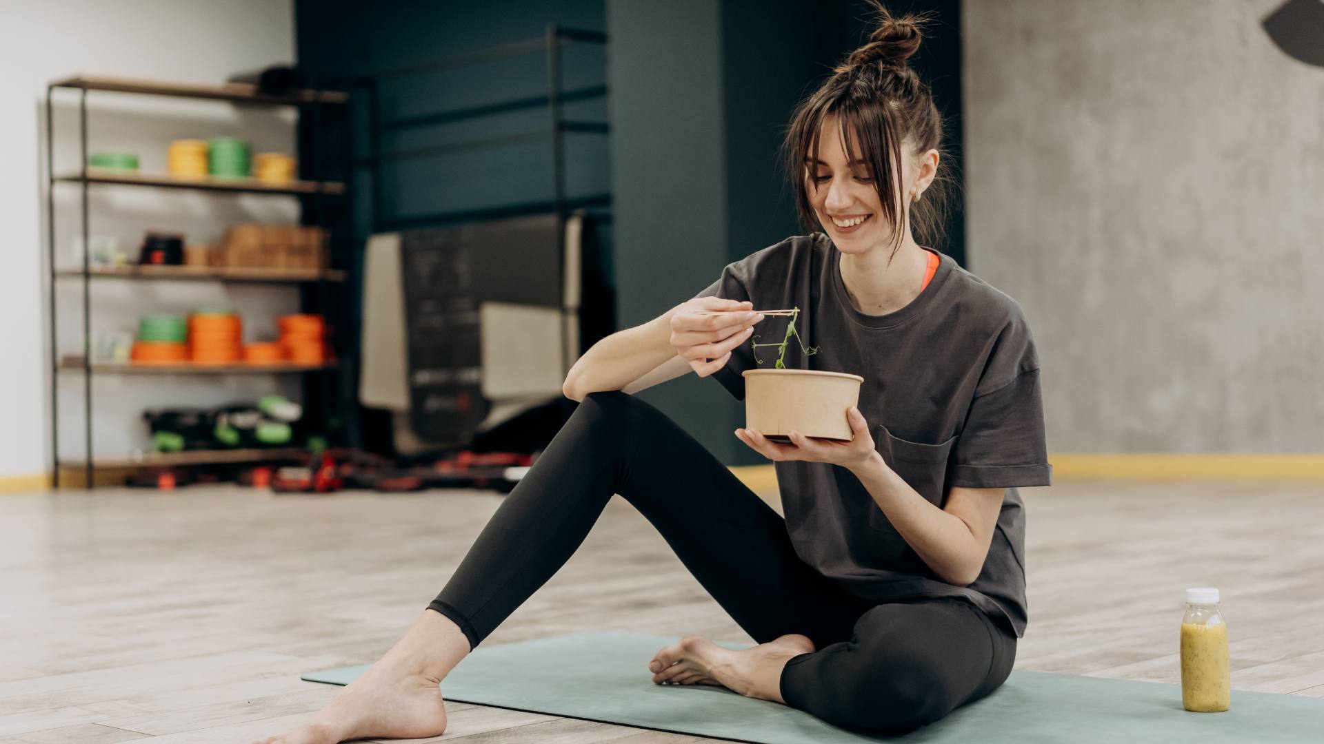 An image of a woman sitting on her yoga mat eating a healthy meal. She's healing her slow metabolism.