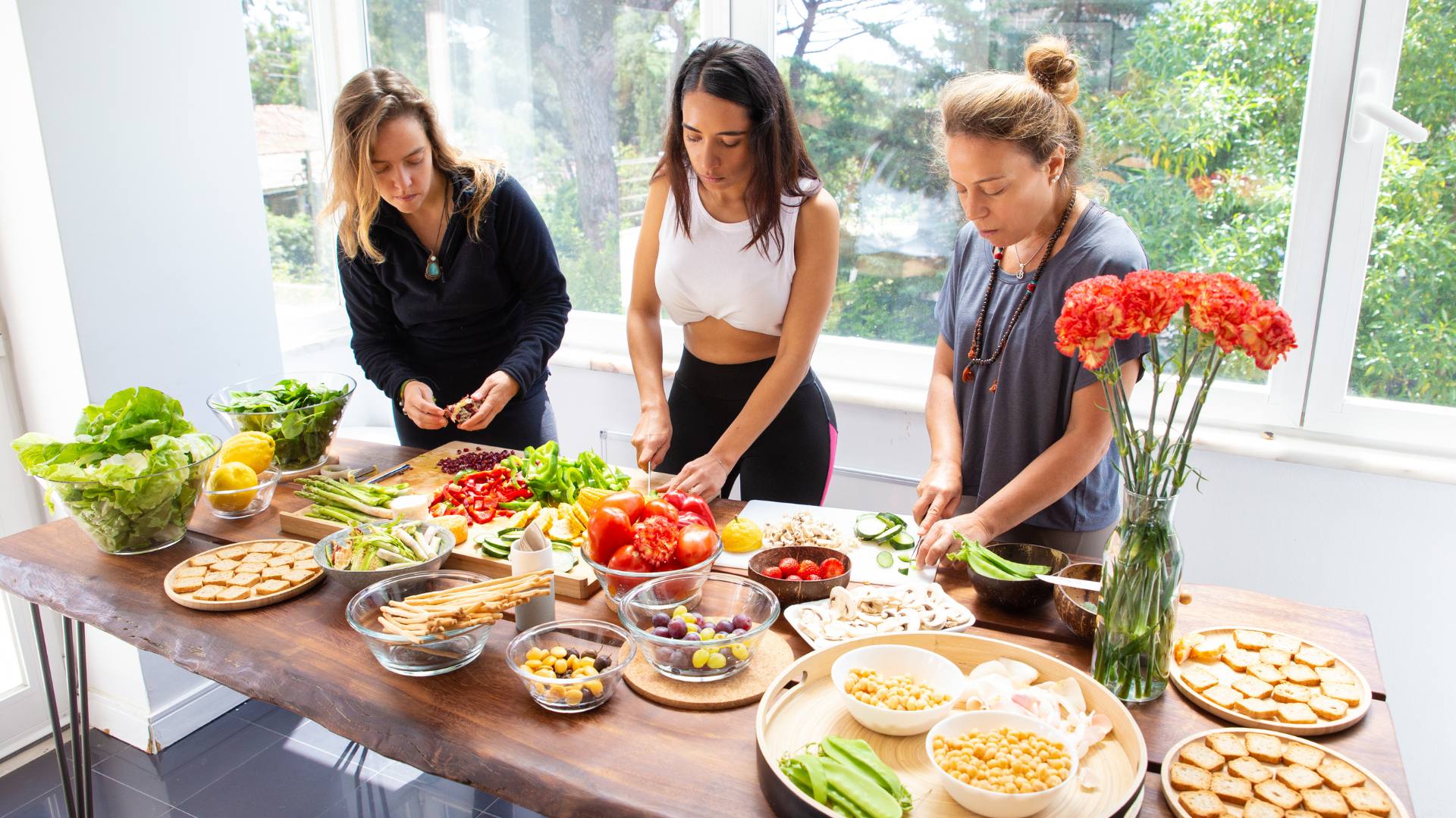 Three women standing over a table of abundant, healthy food. They're not counting calories to lose weight.