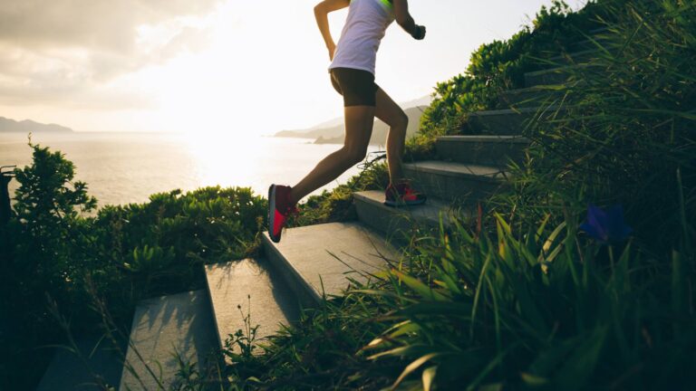 A women runs up the stairs. She is surrounded by greenery and the ocean in the distance. She is demonstrating a healthy weightloss tactic.